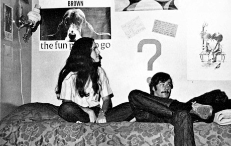 Archival image of two students sitting on a bed in a dorm room