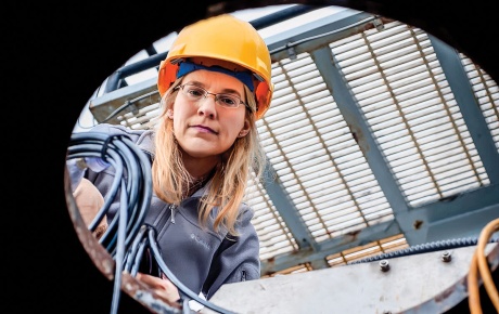 Image of Kelly Benoit-Bird looking down a manhole with a hard hat on.