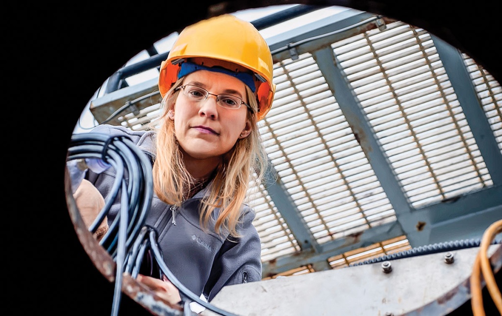 Image of Kelly Benoit-Bird looking down a manhole with a hard hat on.