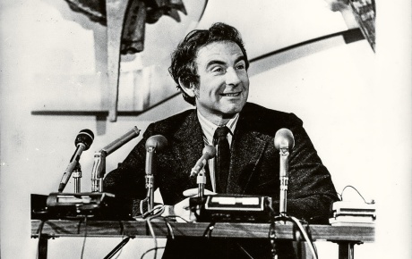Archival image of Leon Cooper sitting at table with microphones in front of him.