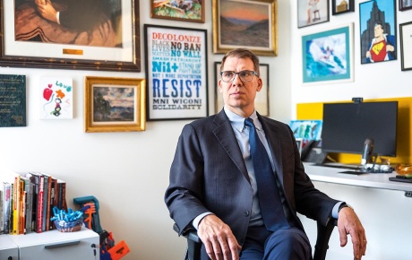 Image of Matthew Guterl sitting in a chair with a wall full of art behind him.